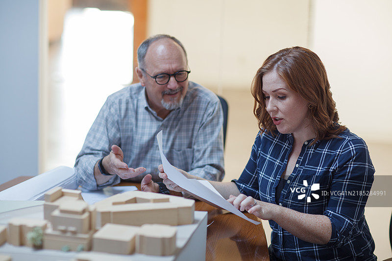 中年女性在城市规划办公室的团队会议中与资深同事讨论建筑计划图片素材