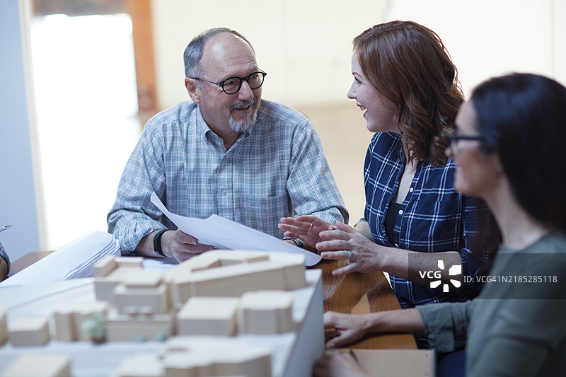 中年女性与资深男性设计师同事在城市规划办公室讨论建筑计划，团队合作会议。图片素材