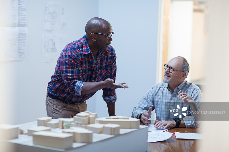 一位成熟的黑人男性与年长的男性设计师同事在城市规划办公室讨论建筑计划，进行团队合作会议。图片素材