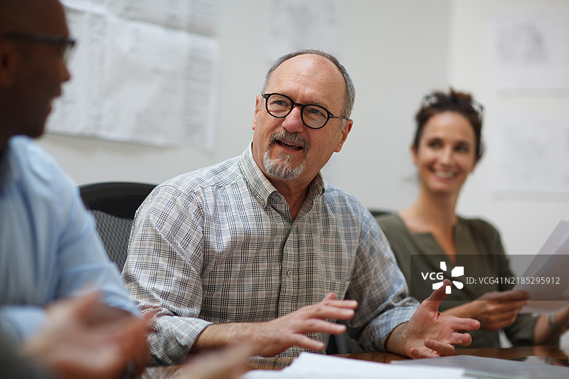 一位年长男性在设计办公室的会议中与同事们坐在桌旁解释。图片素材
