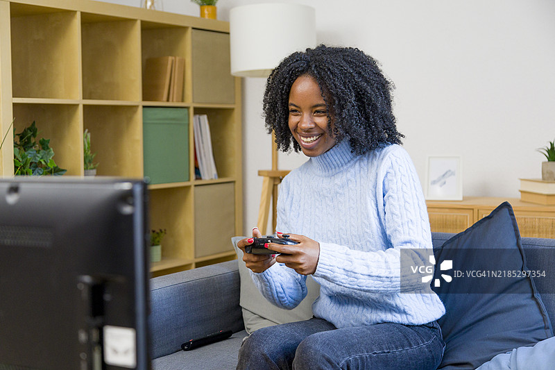 年轻女性坐在沙发上玩电子游戏，手握控制器图片素材