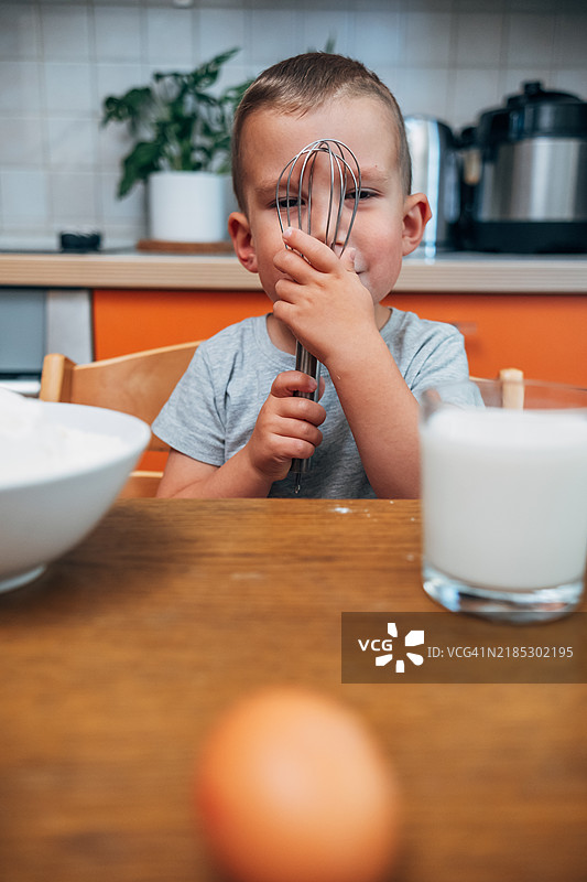 可爱的四岁男孩在家里的厨房里手握打蛋器，准备搅拌面团，正在做早餐。图片素材