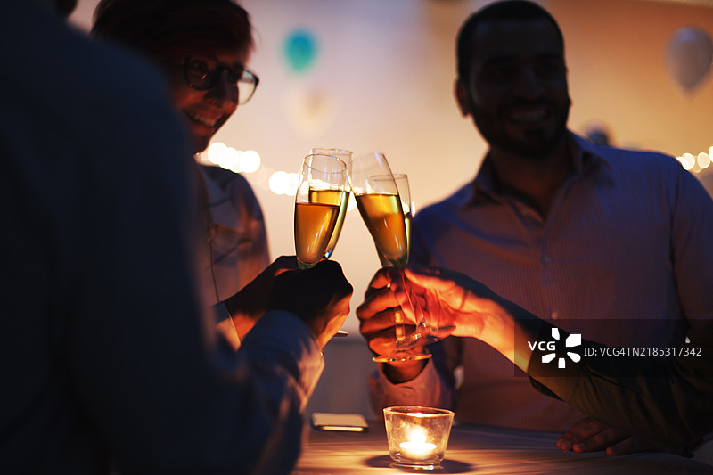 多种族朋友在烛光接待派对的社交活动中共同举杯庆祝香槟。图片素材