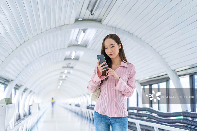 亚洲女性在现代人行天桥上走路时使用手机图片素材