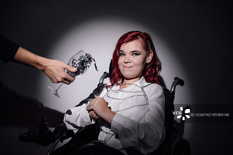 年轻女性在社交聚会上享用闪亮饮料，坐在轮椅上，背景是晚间活动。图片素材