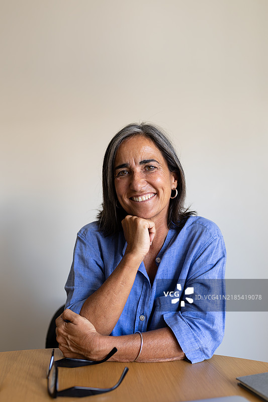 微笑的成熟职业女性坐在桌子前，戴着眼镜。图片素材