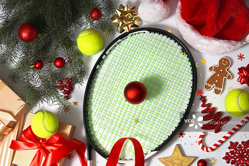 运动快乐的新年和圣诞庆祝活动，包含网球拍、网球、礼品盒、圣诞老人帽、松树枝和白色背景上的圣诞装饰。图片素材
