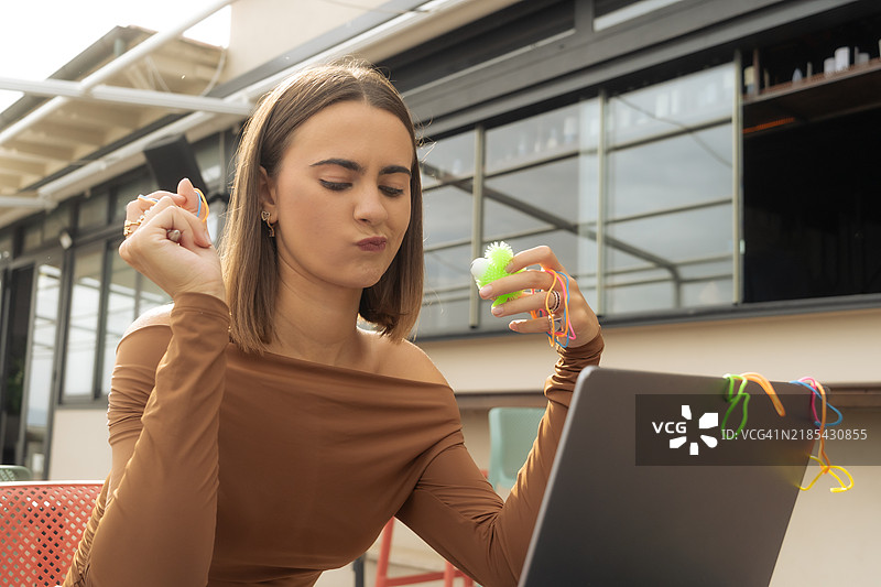 年轻女性在使用电脑，做笔记，并利用橡皮筋、玩具和辅助设备来提高专注力。图片素材