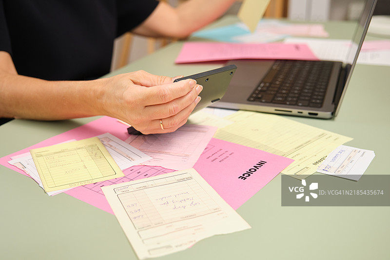会计师使用计算器和笔记本电脑计算税款，桌上有发票。图片素材