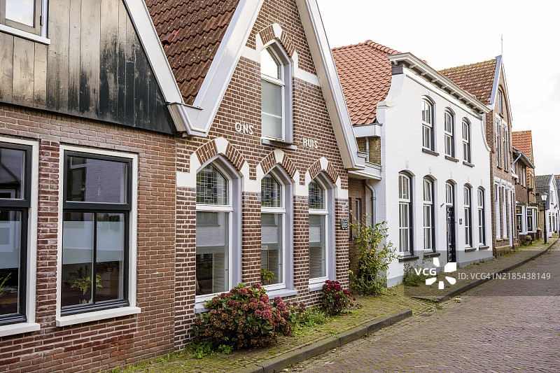 德霍恩，特塞尔，宁静村庄街道旁的传统砖房，醒目的窗户和红色屋顶。图片素材