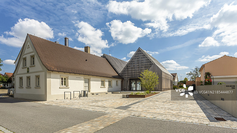 一座传统房屋与现代建筑并排而立，清澈的蓝天下，乡村环境中有一块铺砌的前院，位于上弗兰肯的冈德尔斯海姆。图片素材