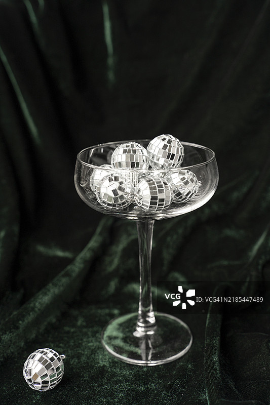 香槟杯里装满了镜面迪斯科球装饰，背景是绿色天鹅绒。新年派对概念。图片素材