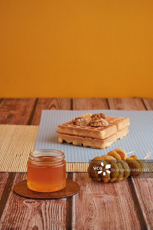 一份健康的早餐，包含华夫饼、核桃和有机蜂蜜，摆放在木桌上。图片素材