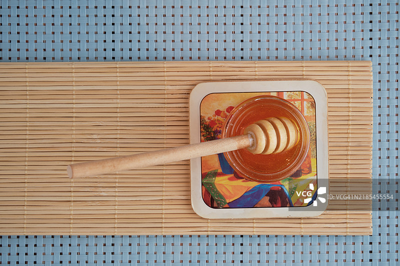 从上方俯视的有机蜂蜜，配有木制蜂蜜搅拌棒，放在蓝色背景下的木桌上。图片素材