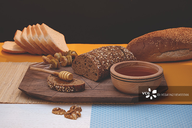 全麦面包和水果，坚果和有机蜂蜜放在木桌上，背景为黑色。图片素材