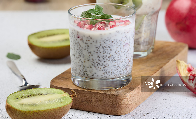 两杯撒有新鲜水果、石榴籽和猕猴桃片的奇亚籽酸奶甜点图片素材