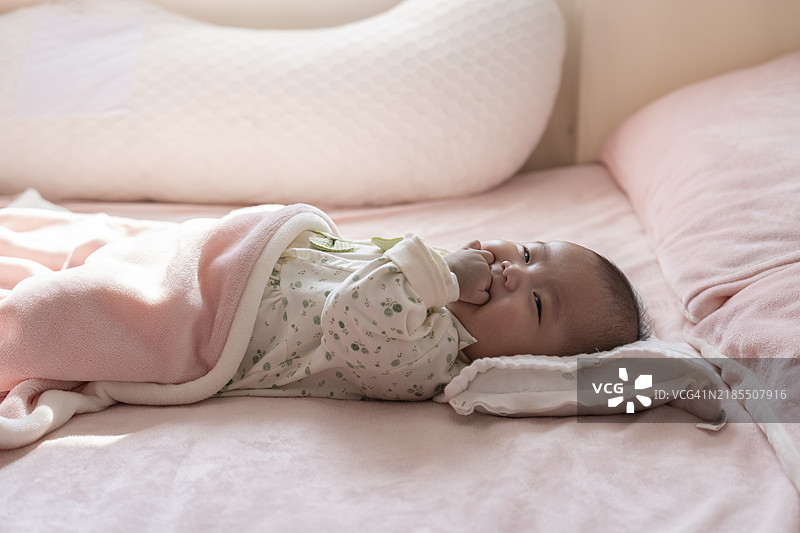 婴儿躺在床上吮吸自己的手图片素材