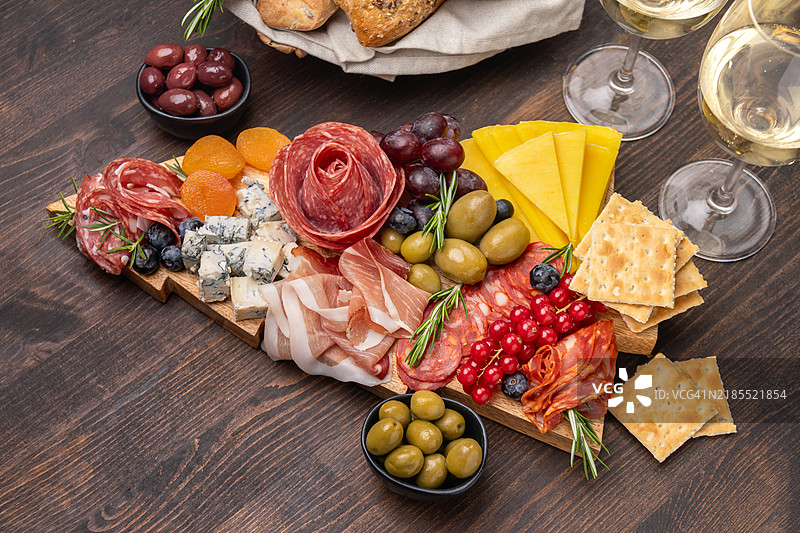 派对食品宴会拼盘，意大利冷切拼盘，火腿、萨拉米香肠、奶酪和面包棒以圣诞树的形状呈现，旁边配有白葡萄酒、普罗塞克或香槟以及节日装饰。图片素材