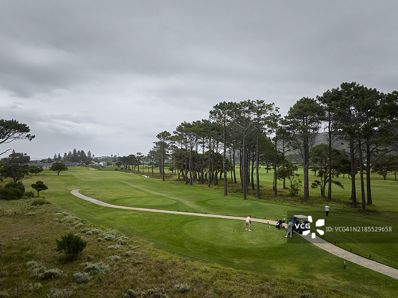 一群老年高尔夫球手在阴云密布的高尔夫球场上开球。图片素材