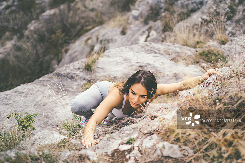 专注的女性在户外自然环境中攀爬岩石边缘图片素材