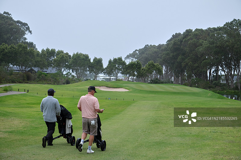 高尔夫球手在阴云密布的日子里走在郁郁葱葱的球道上图片素材
