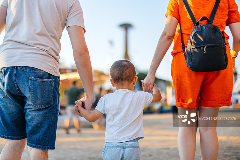 年轻父母带着他们的儿子在游乐园散步的背影图片素材