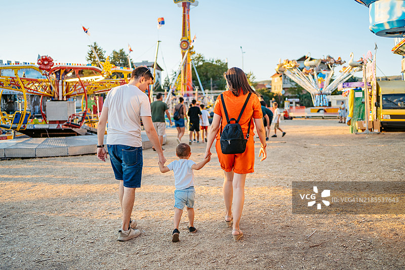 年轻父母带着他们的儿子在游乐园散步的背影图片素材