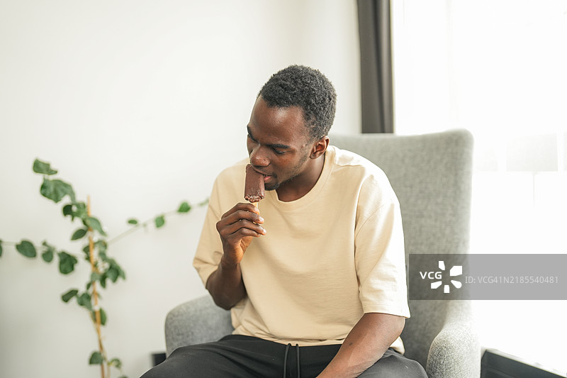 年轻黑人男性因在家沙发上咬冰淇淋而感到牙齿敏感，正在忍受牙痛。图片素材
