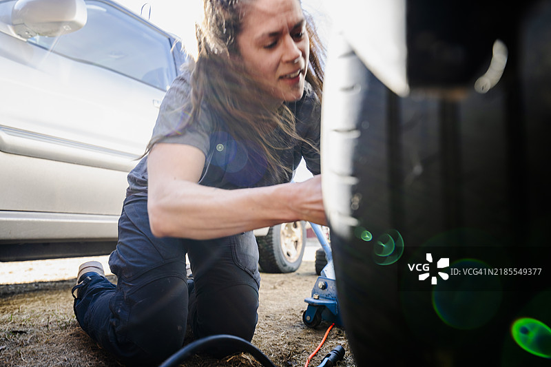女性修理工在阳光明媚的日子里更换汽车轮胎图片素材