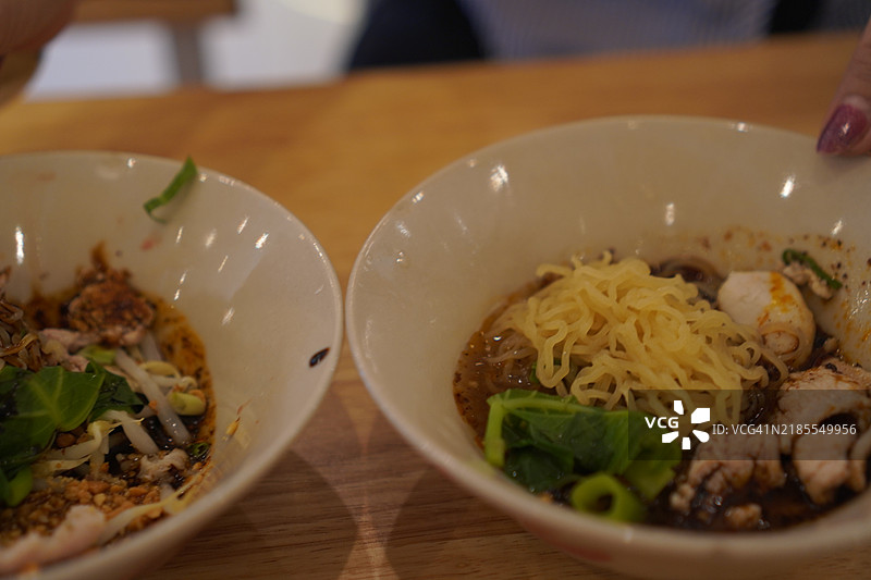 泰式面条，白碗中盛着小面条、炖猪肉、肉丸、猪肝和血汤，搭配木筷和勺子，调味后美味的泰国菜。图片素材