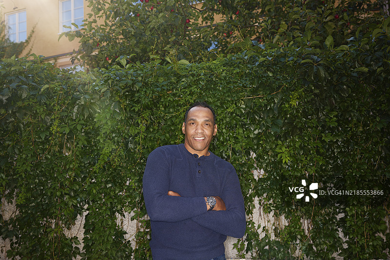 微笑的男性双臂交叉，站在常春藤墙前图片素材