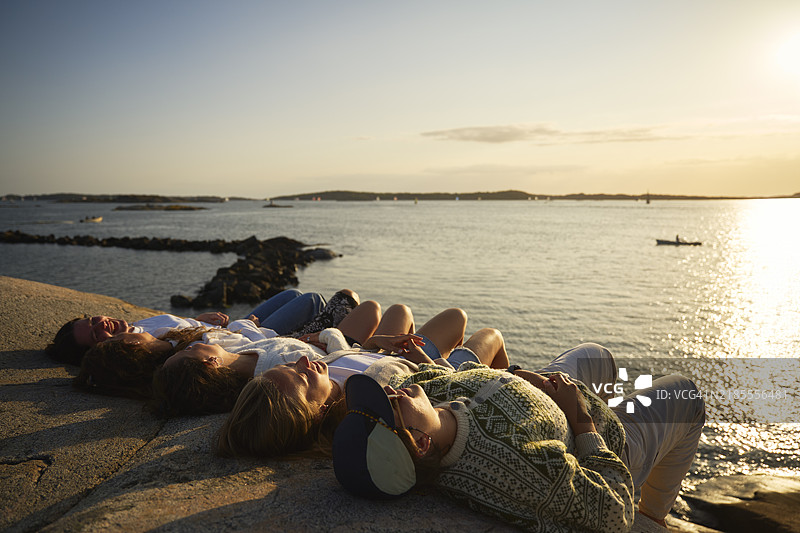一群女性朋友在湖边的岩石上躺着，享受日落时光图片素材