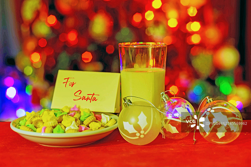 一杯牛奶和糖饼干，桌上还有给圣诞老人的便条，背景是模糊的圣诞灯光。图片素材