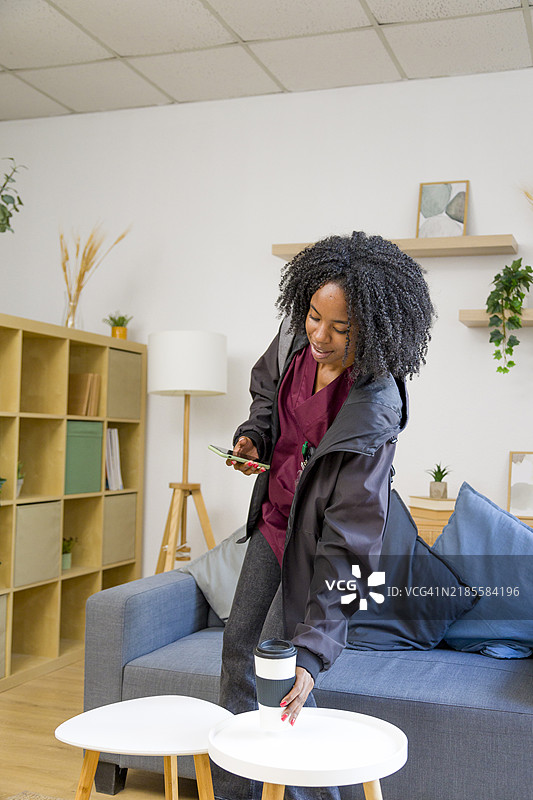 年轻女性在桌子上放咖啡，同时使用智能手机图片素材