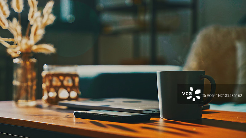阳光洒在公寓里的桌子上，桌上有咖啡、手机和笔记本电脑图片素材