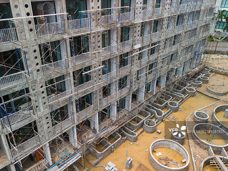 一个建筑工地，展示了多层建筑上的脚手架和泥泞区域中的圆形混凝土基础。图片素材