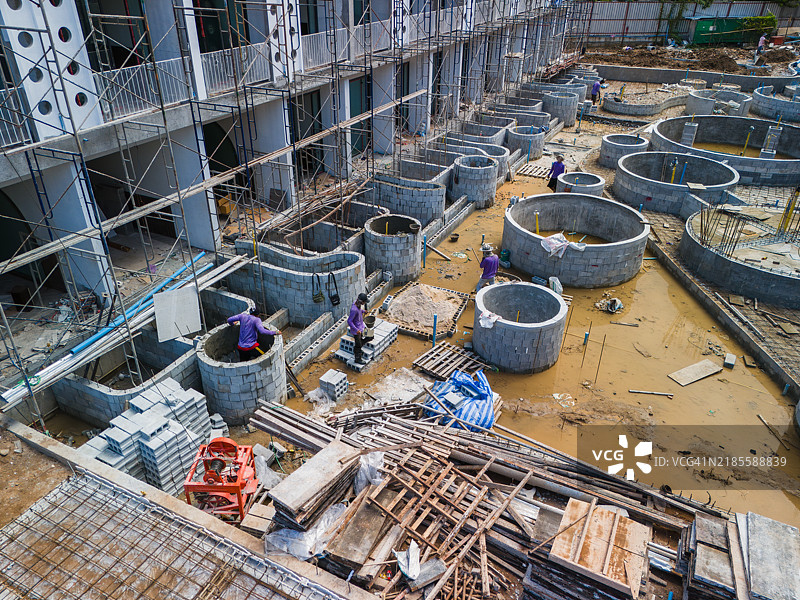 建筑工人在一个有脚手架、材料和泥泞地面的工地上组装圆形混凝土基础。图片素材