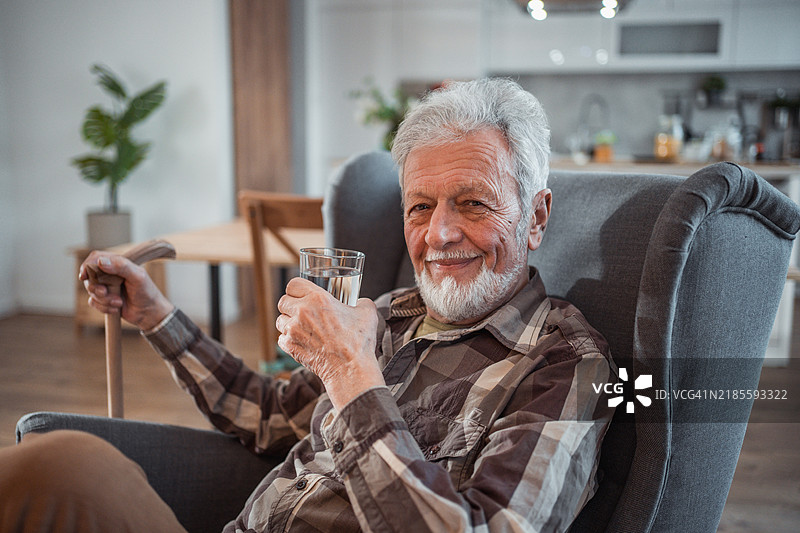 在他的扶手椅上，老人悠闲而安详地喝着一杯水，而外面的世界则喧嚣不已。图片素材