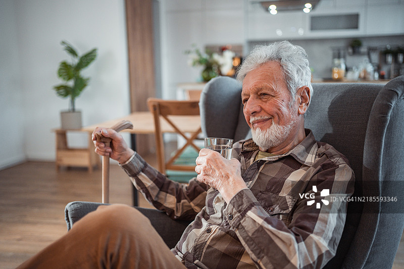 在他的扶手椅上，老人悠闲而安详地喝着一杯水，而外面的世界则喧嚣不已。图片素材