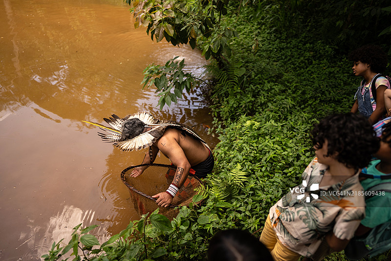 土著男子在巴西的土著部落进行实地考察时教孩子们可持续捕鱼。图片素材