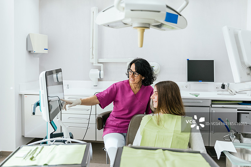 牙医在牙科诊所向年轻患者展示监视器上的结果图片素材