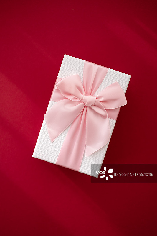 红色背景上的装饰礼品盒，配有粉色丝带，适合特殊场合和庆祝活动图片素材