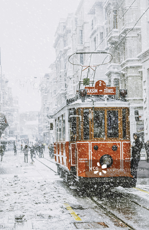 怀旧的红色电车在土耳其伊斯坦布尔贝尤鲁区塔克西姆的伊斯提克拉尔大街上大雪纷飞。图片素材
