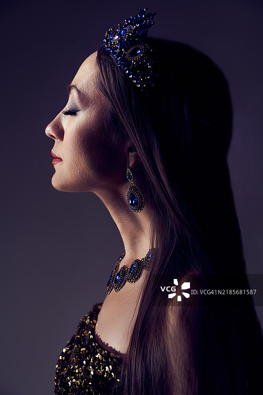 一位戴着蓝色王冠、项链和耳环的女性侧面，双眼闭合。图片素材