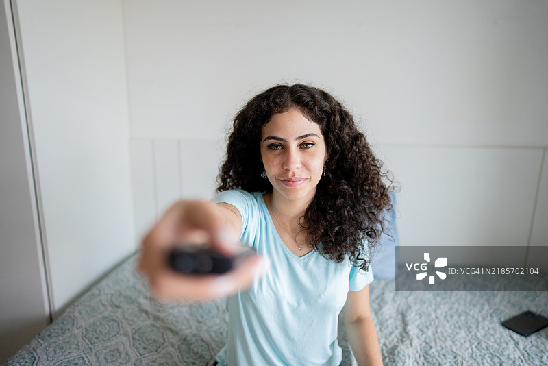 年轻女性在公寓里使用遥控器观看电视 - 从电视的视角看图片素材