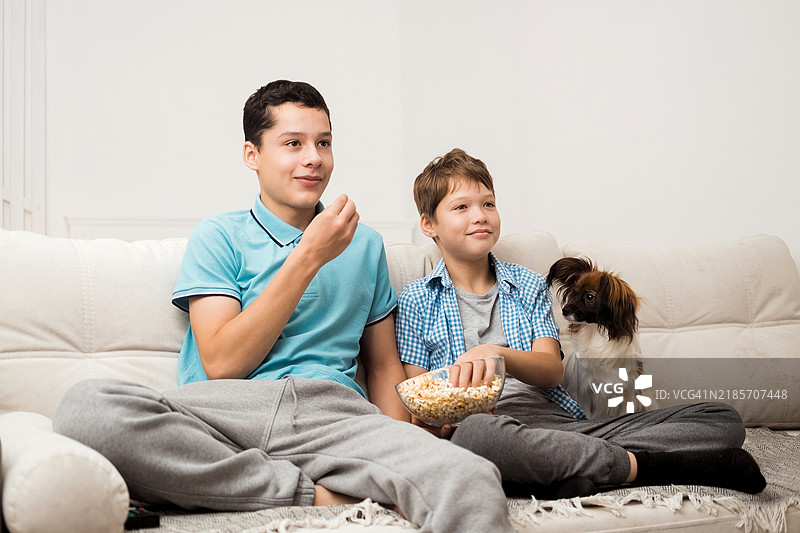 快乐的孩子们坐在客厅的沙发上，看电视并吃着爆米花。图片素材