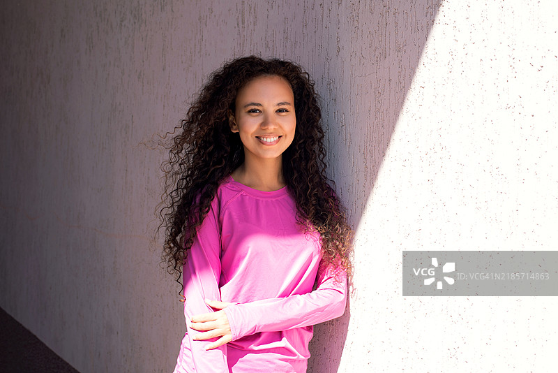 穿着运动服的深肤色女性肖像。美丽的深肤色女孩在街上。健康的生活方式。深肤色女性在街道旁的墙壁附近的肖像。图片素材