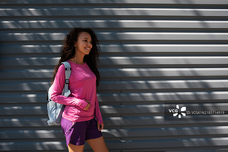 穿着运动服的深肤色女性肖像。美丽的深肤色女孩在街上。健康的生活方式。深肤色女性在街道旁的墙壁附近的肖像。图片素材