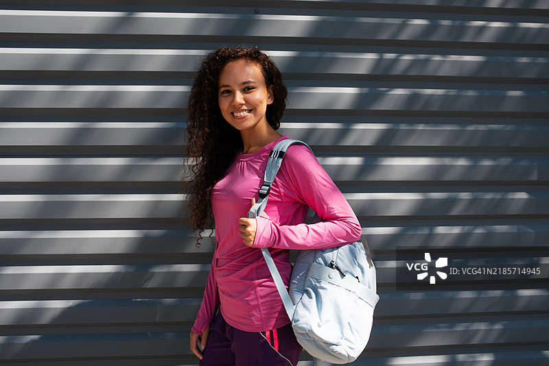 穿着运动服的深肤色女性肖像。美丽的深肤色女孩在街上。健康的生活方式。深肤色女性在街道旁的墙边肖像。图片素材