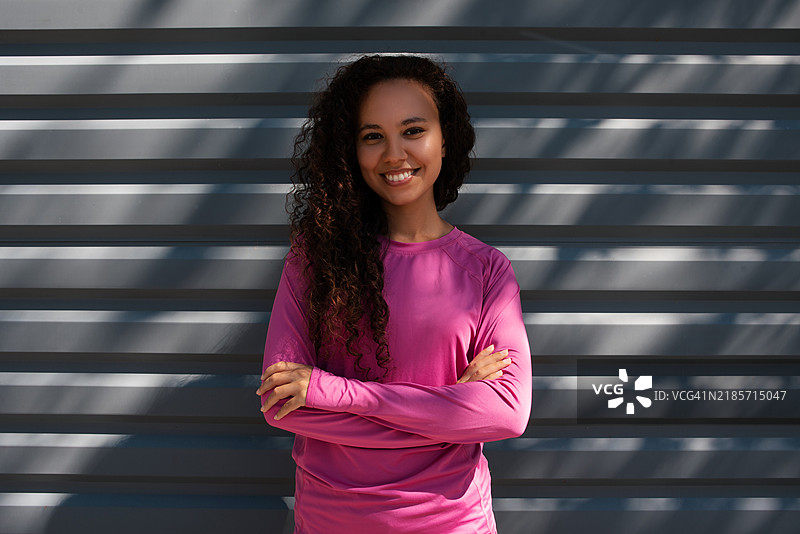 穿着运动服的深肤色女性肖像。美丽的深肤色女孩在街上。健康的生活方式。深肤色女性在街道旁的墙壁附近的肖像。图片素材